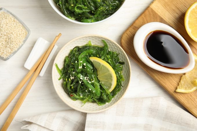 Japanese seaweed salad with lemon slice served on white wooden table