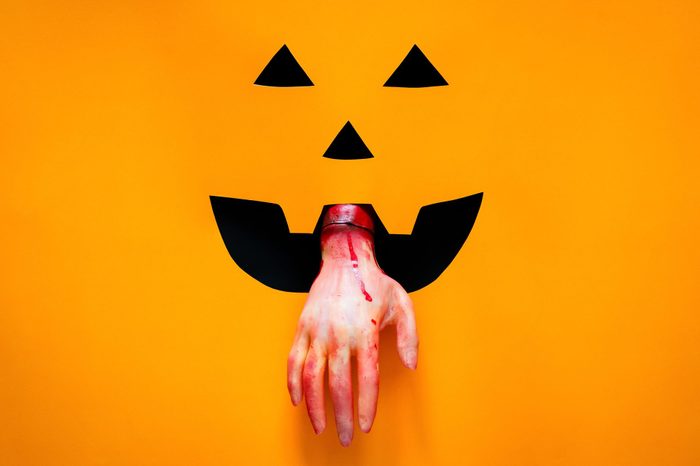 Halloween pumpkin face background with hand sticking out of the mouth. the hand has fake wounds and fake blood