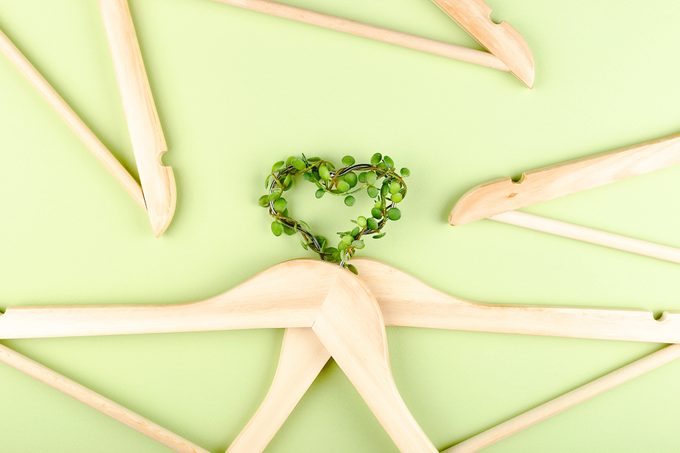 leaves on hanger in the shape of a heart to representConscious consumption of clothes slow fashion concept. Heart of clothes hangers entwined with plant on green background