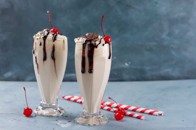 two chocolate Milkshakes in a glass with straws and cherries