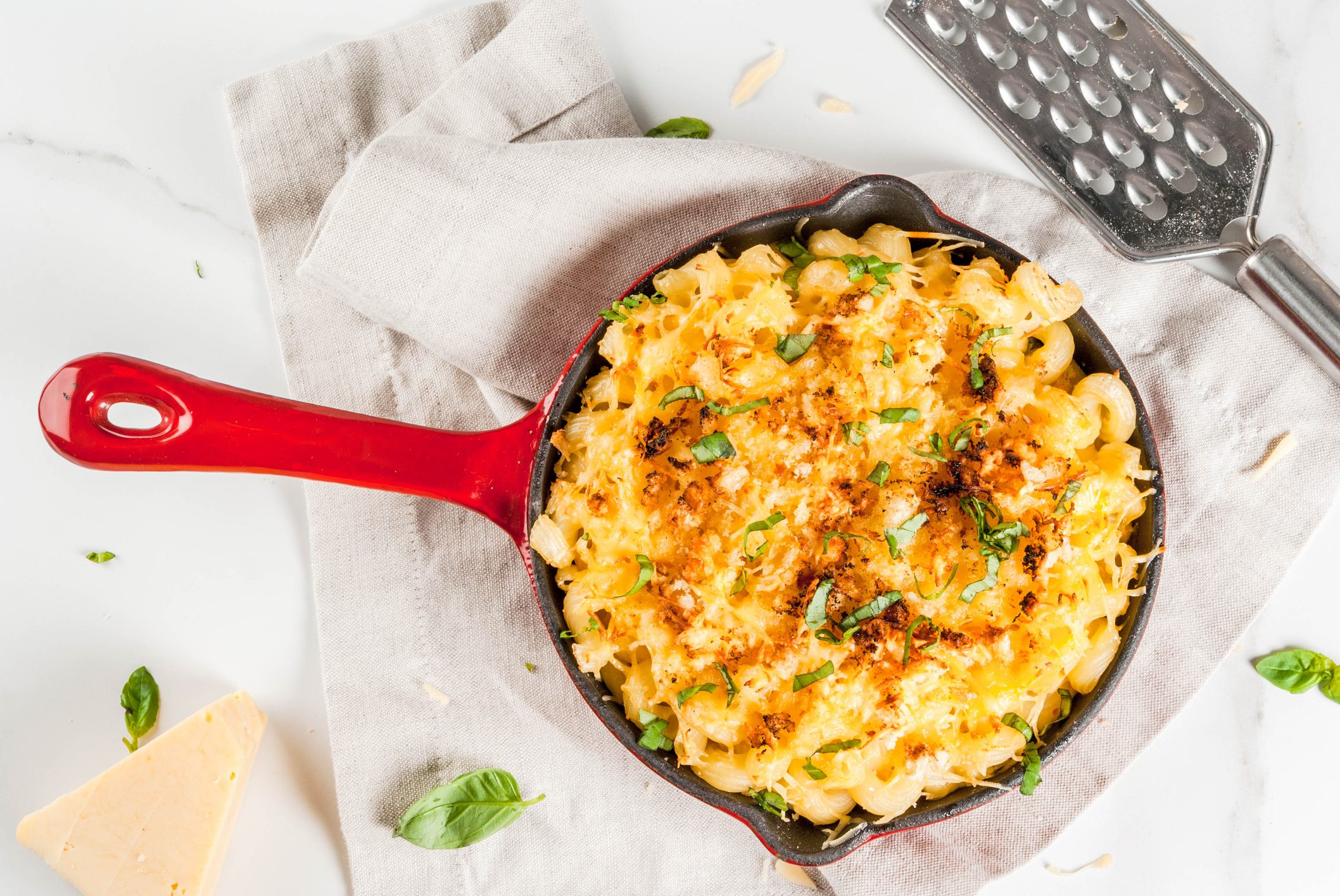 Mac and cheese, american style macaroni pasta with cheesy sauce and crunchy breadcrumbs topping, in portioned pan, white marble table