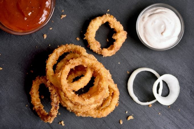Fried onion rings with sauce on black stone background