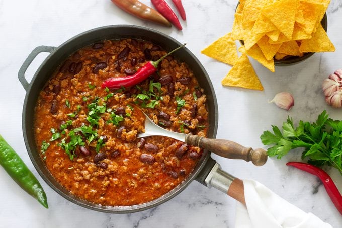 Chili con carne in a pan served with nachos, pepper and herbs
