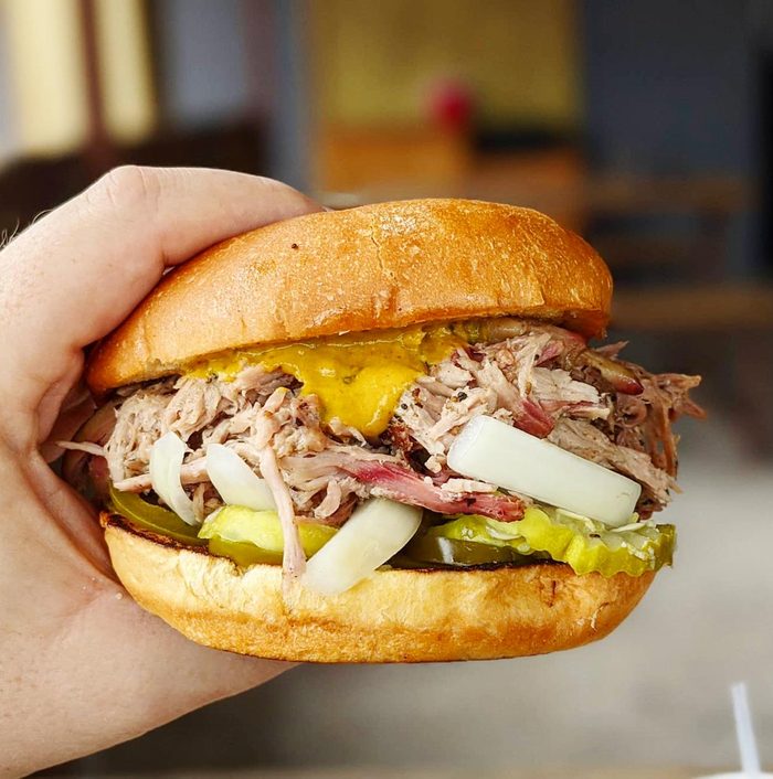 hand holding a pulled pork sandwich with mustard