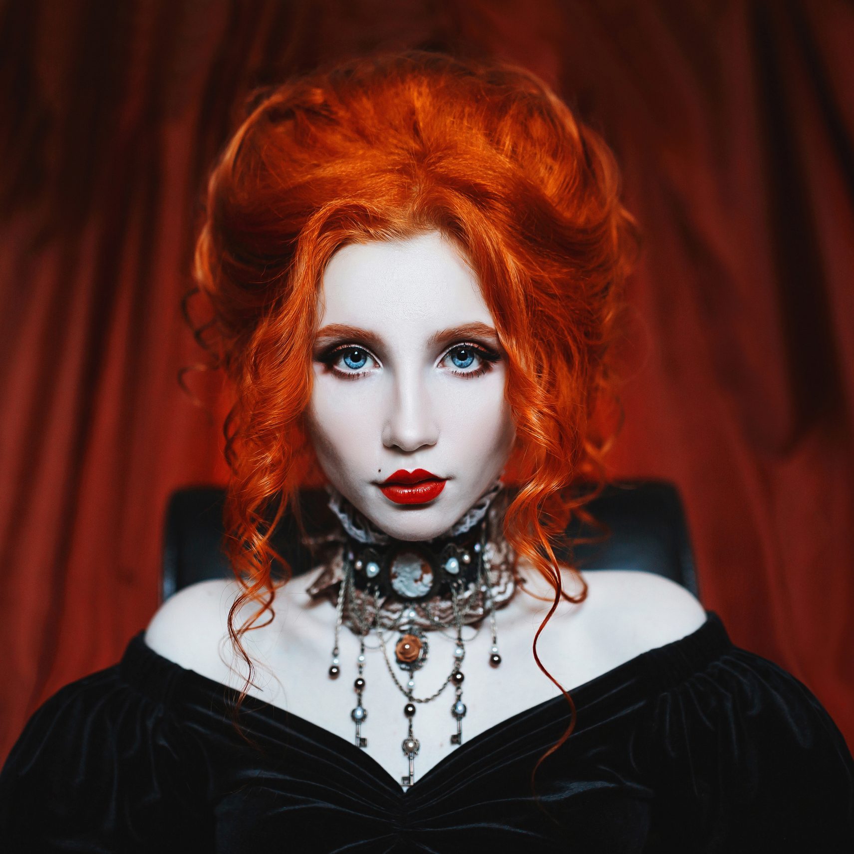 Gothic woman is a vampire with pale skin and red hair in a black dress and a necklace on her neck. Girl witch with vampire claws and red lips. Gothic look. Outfit for halloween.