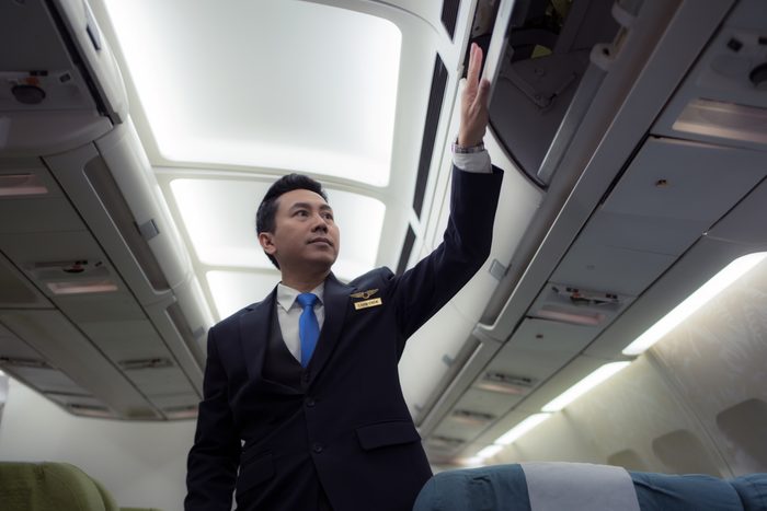 Confident Asian male pilot in uniform standing at the passenger seat inside of the airplane .