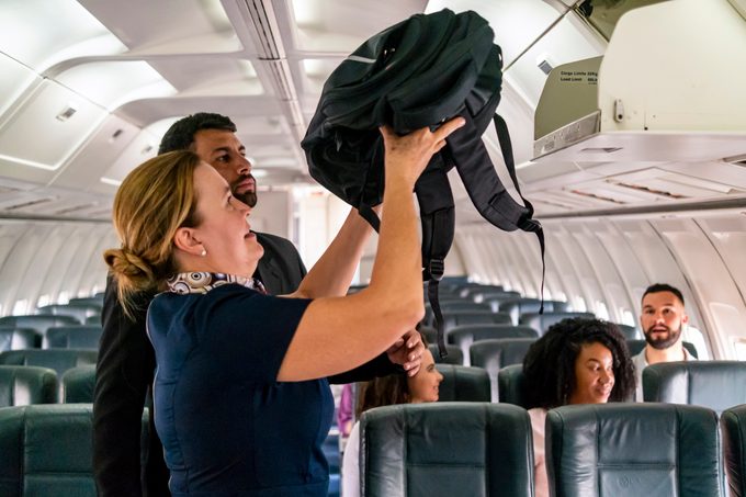 flight attendant helping a passenger with their carryon