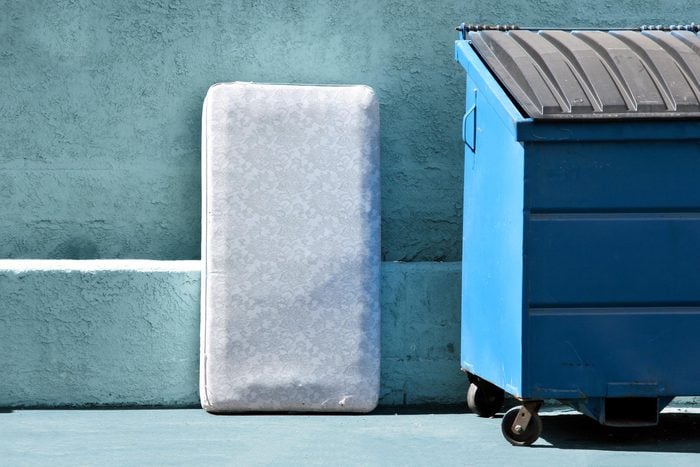 mattress next to a blue recycling bin outside