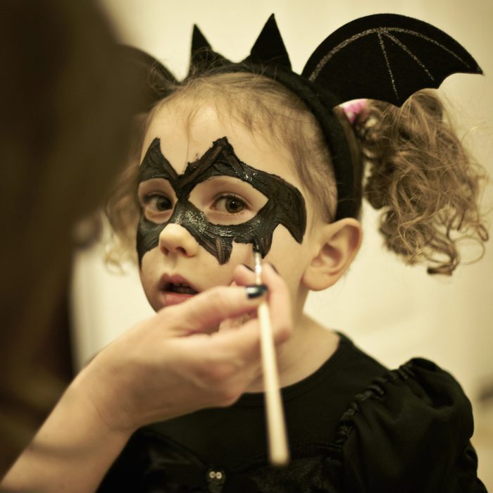 Mother painting daughters face for halloween bat costume