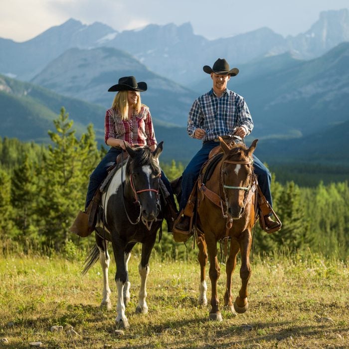 Cowboy and cowgirl ride horse thru mountain meadow