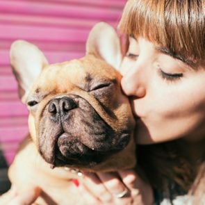Portrait of young woman kissing French bulldog