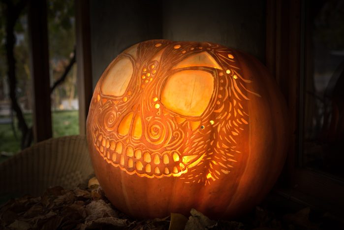 Artistically carved glowing jack-o'-lantern on tabletop display with leaves for Hallowe'en