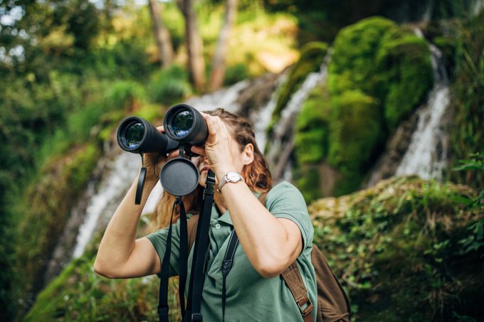 Explorer with binoculars by the waterfall in the middle of the rain forest