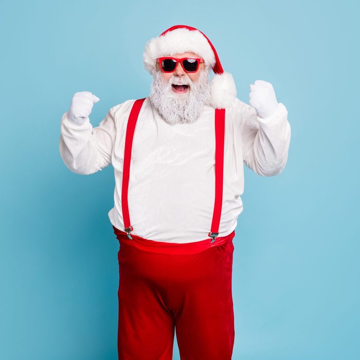 Portrait of funny funky fat santa claus with big belly raise fists scream yeah have luck celebrate newyear x-mas party wear suspenders modern red spectacles isolated over blue color background
