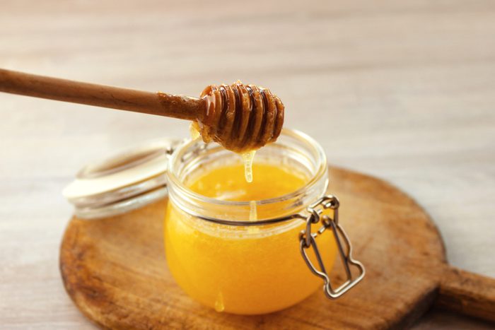 Honey dripping from a wooden dipper in jar on old cutting board on white wooden rustic background