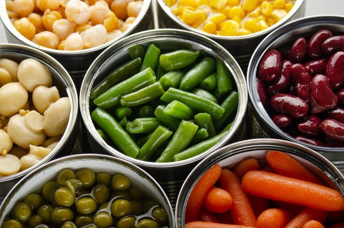 Canned vegetables in opened tin cans on kitchen table. Non-perishable long shelf life foods background
