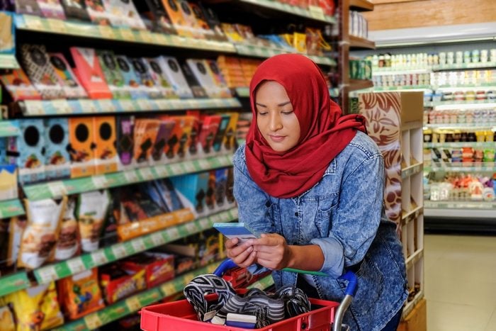 Front view shot of Malaysian woman with a hijab, holding a chocolate bar, while reading the nutrition label on the back of the packaging.
