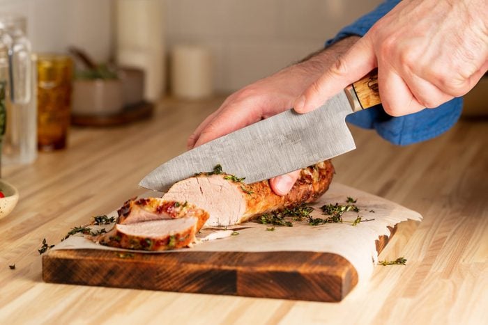 Unrecognizable Man Cuting With Large Knife Baked Pork Tenderloin On Cutting Board
