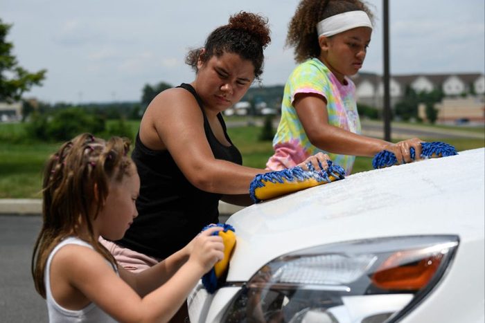 Volunteers Lily Frey, 6, left, with Ashia Ortiz, 16, and Jannah Green, 14, right, scrub a hood during a car wash fundraiser to support the purchase of a service dog for autistic teen Seth Oran, 15, of Sinking Spring. Held at Discovery Credit Union in Spri
