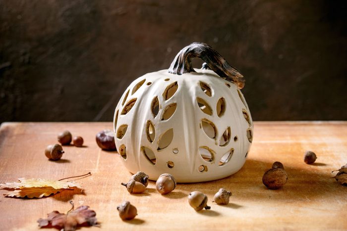 Halloween or Thanksgiving decorations, white handcrafted carved ceramic pumpkin standing on orange stone table with autumn leaves and acorns, Halloween holiday interior home decor, Copy space