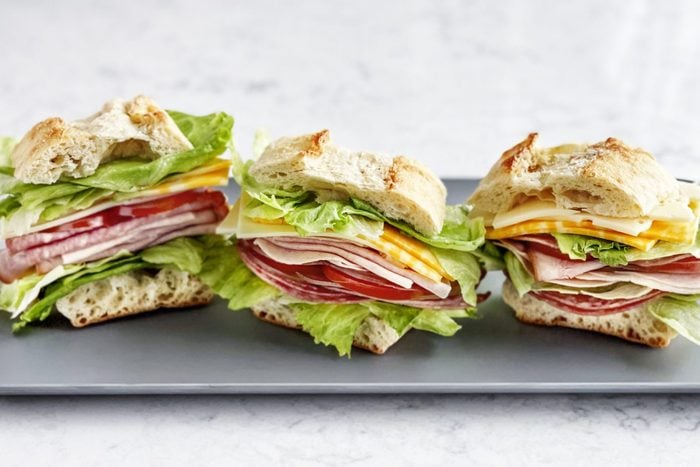 Sandwiches with salami, ham, cheese, and tomatoes on a tray on white background