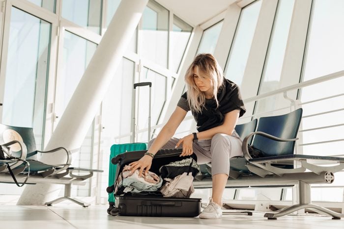 Blond serious woman with luggage sitting in waiting room at the international airport, packing suitcase with clothes