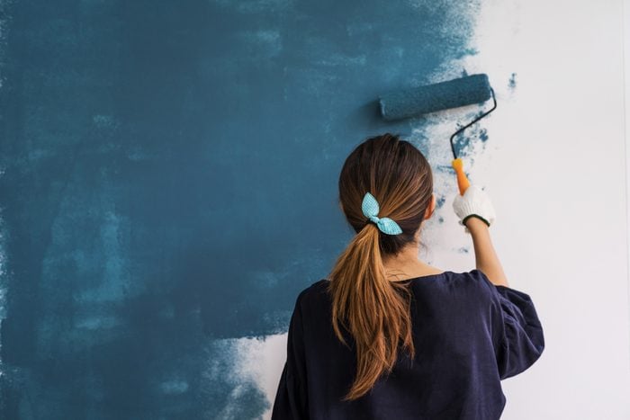 Young woman painting interior wall with paint roller and teal paint in a new house