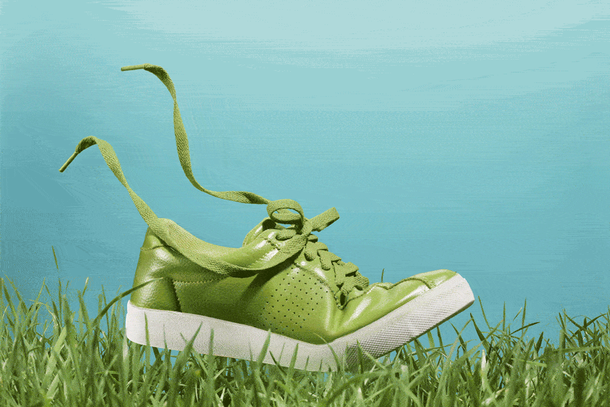 Green Sneaker with floating laces in the grass with blue background