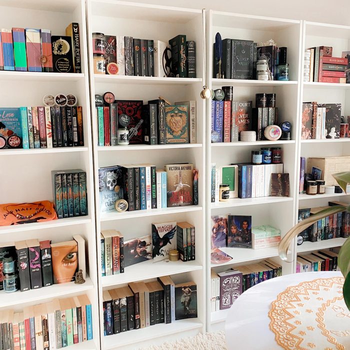4 tall white bookshelves lining a wall filled with books in an organized way