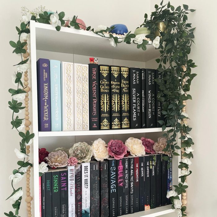 a small section of a white bookcase decorated with fake flowers and a vine plant