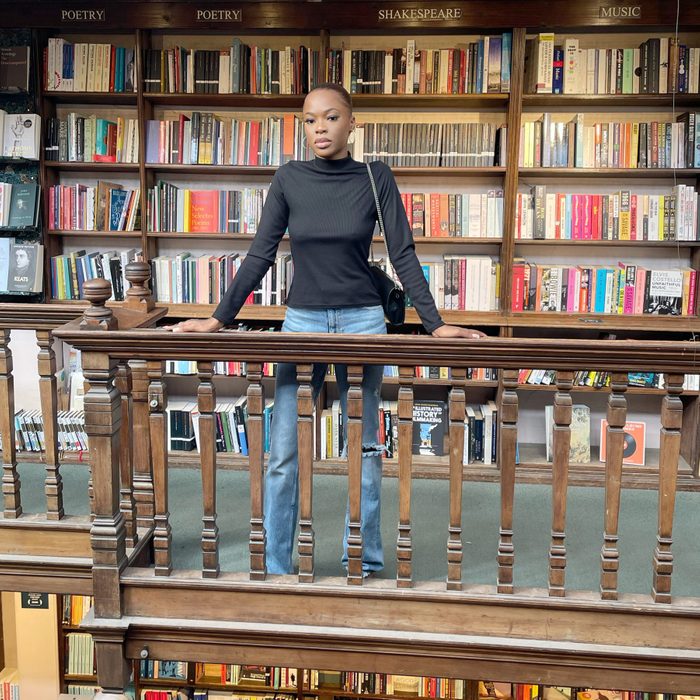 a woman stands on the top floor of a bookstore with labeled shelves behind her