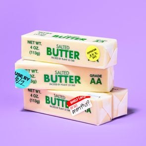 four sticks of butter stacked against purple background. three of the sticks have various expiration stickers