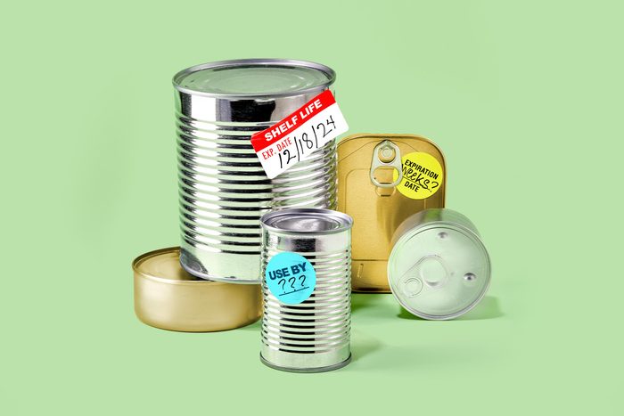 Canned Food arranged on a green background. some cans have expiration stickers