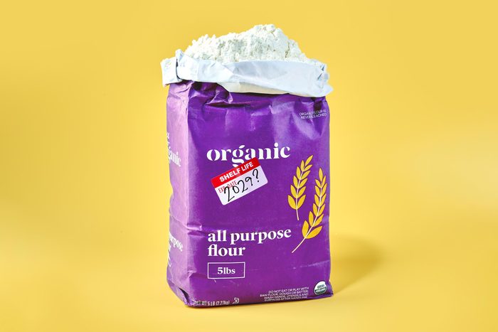 opened bag of flour on yellow background. the flour package has an expiration sticker on it