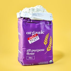 opened bag of flour on yellow background. the flour package has an expiration sticker on it