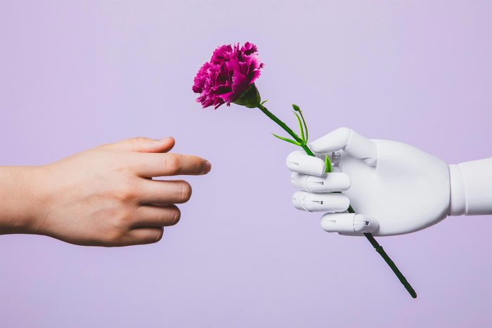 human hand and robot hand extending toward each other. robot hand offering a purple flower
