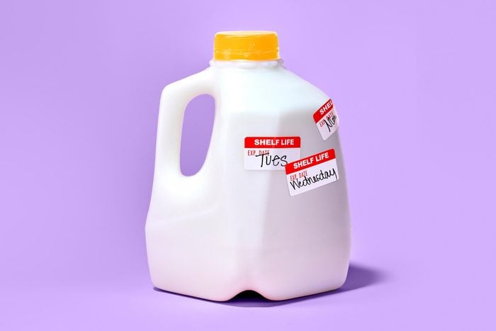 gallon of milk on purple background. the container has three expiration stickers added, each with a different day of the week written on it