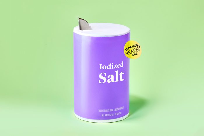 container of salt against green background. the container has an expiration sticker on it.