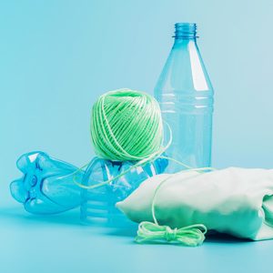 empty water bottles arranged near a ball of thread and a folded item of clothing to imply sustainable clothing made from plastic