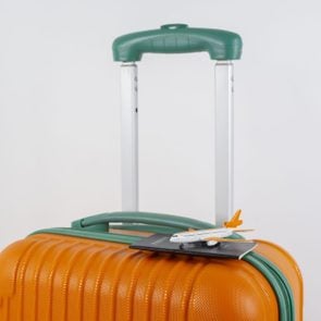 orange and green Travel suitcase with a passport and miniature airplane on the top of the suitcase