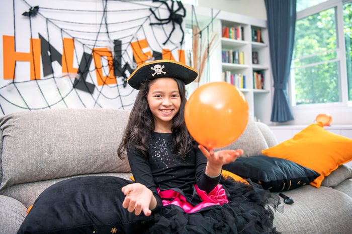 girl dressed in halloween costumes enjoy playing with orange balloon.