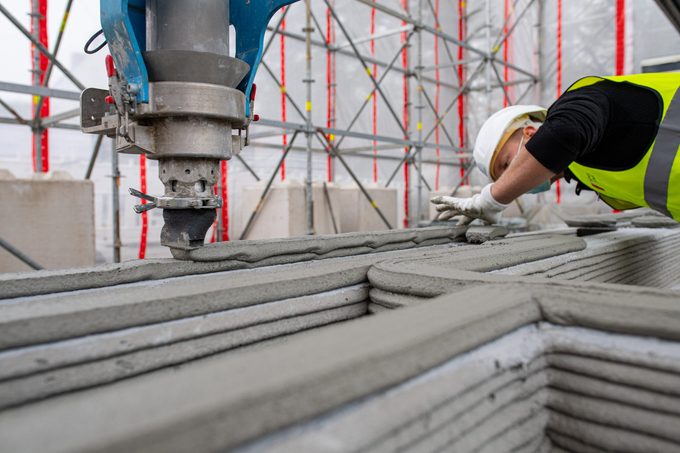 First 3D printed residential building in Germany. An employee of the construction company watches the 3D printer, which applies the next layer of concrete to the walls.