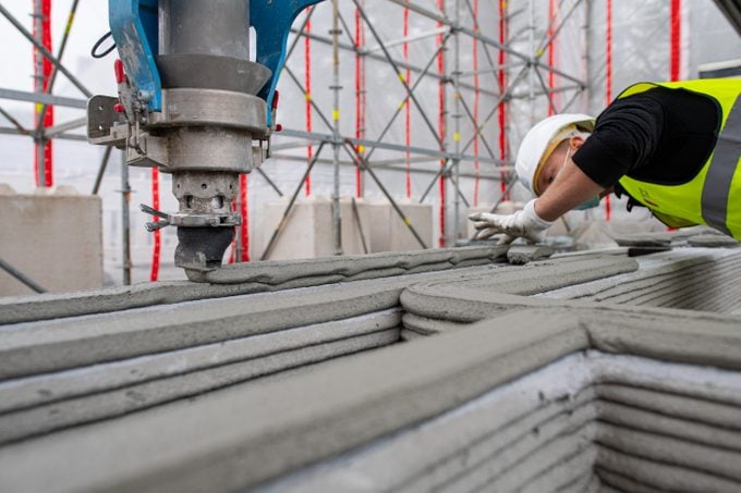 First 3D printed residential building in Germany. An employee of the construction company watches the 3D printer, which applies the next layer of concrete to the walls.