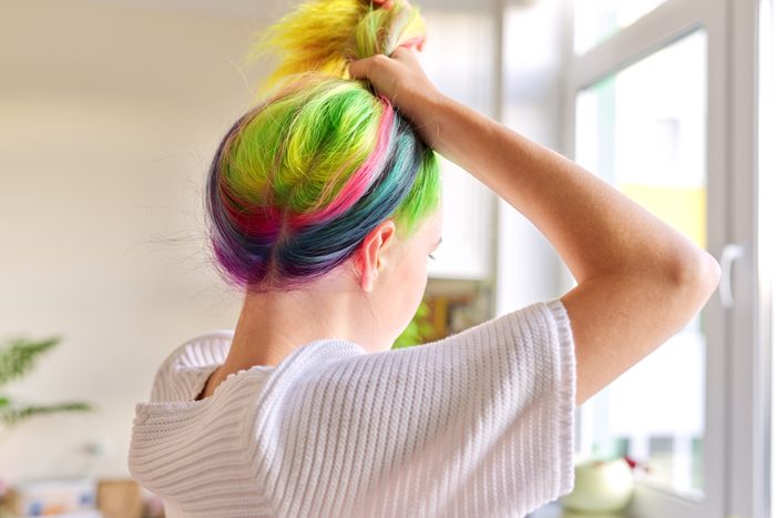 Fashionable girl with trendy rainbow dyed hair combing hair at home