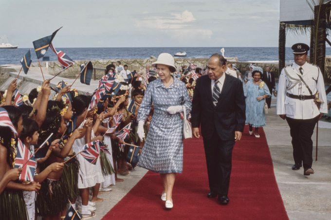British Royal Queen Elizabeth II escorted by an unspecified dignitary alongside a crowd of children waving British flags in Honiara, Solomon Islands, 18th October 1982.