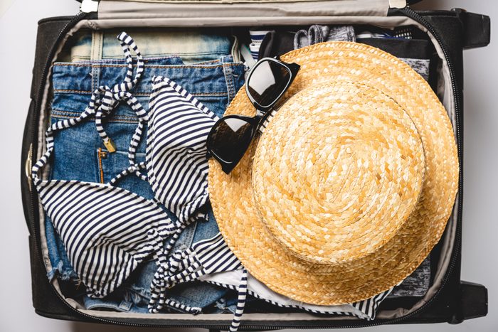 Open travel bag with summer clothes, hat, film camera and passports on white background, top view, flat lay