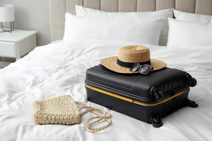 Suitcase packed for cruise trip and summer accessories on bed indoors
