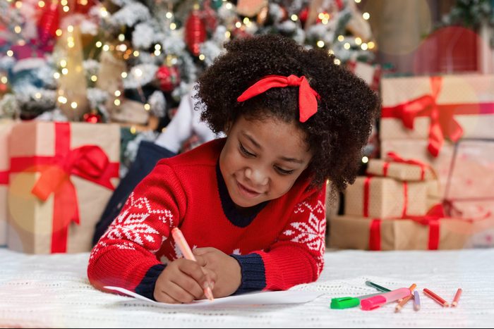 Little black girl lying on floor, writing letter to Santa