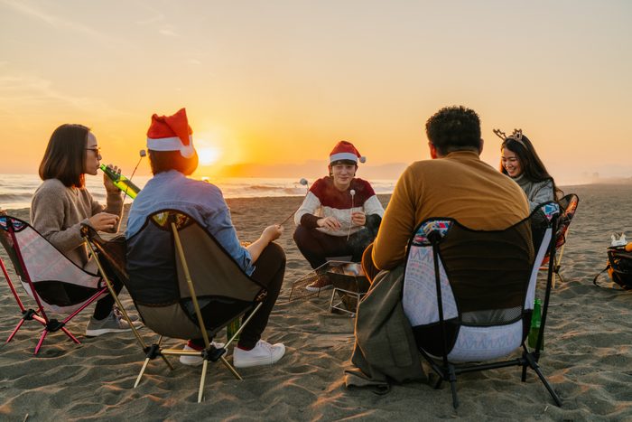 Group of young friends enjoying Christmas party at beach and eating marshmallow