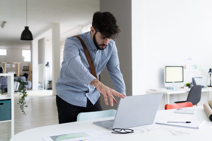 Young businessman closing laptop at desk in creative office